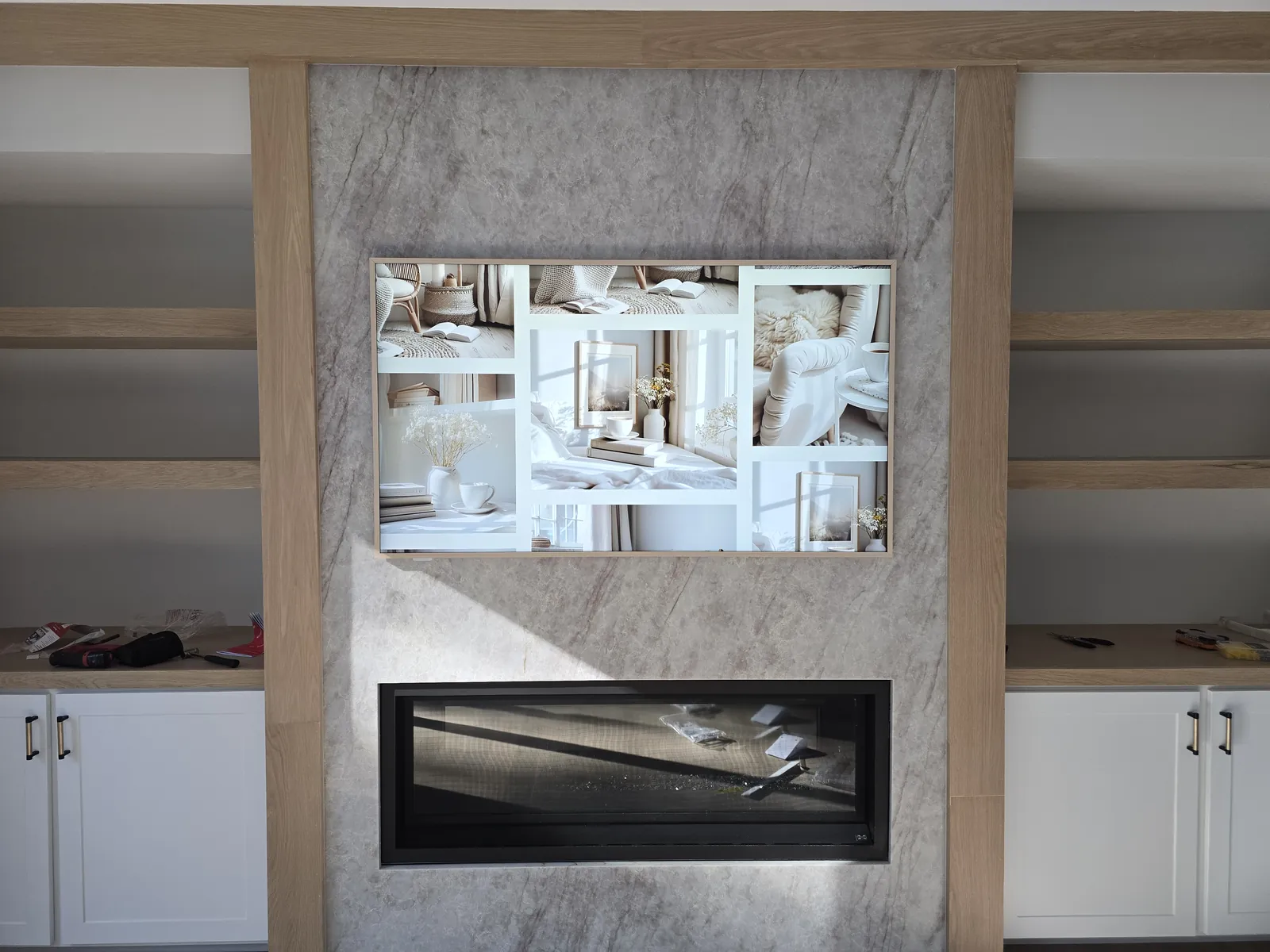 Frame-style TV mounted on a stone fireplace wall between built-in shelves